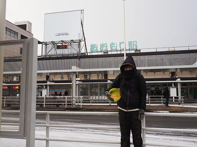 風呂桶片手に青森駅前に立つ毎川直也