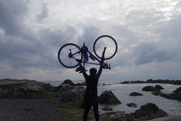 海を背景にロードバイクを持ち上げて自撮りする筆者
