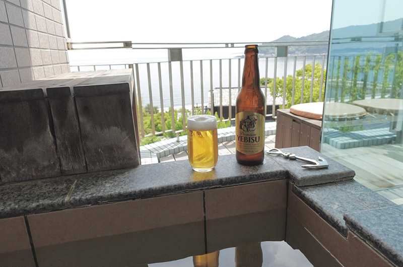 露天風呂の縁に置かれた瓶ビールとグラス