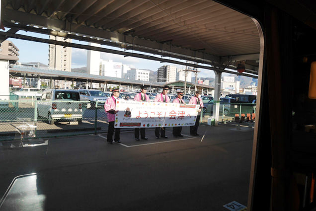 会津若松駅ホームで「ようこそ会津へ」の旗を持った駅員さんが並んでいる